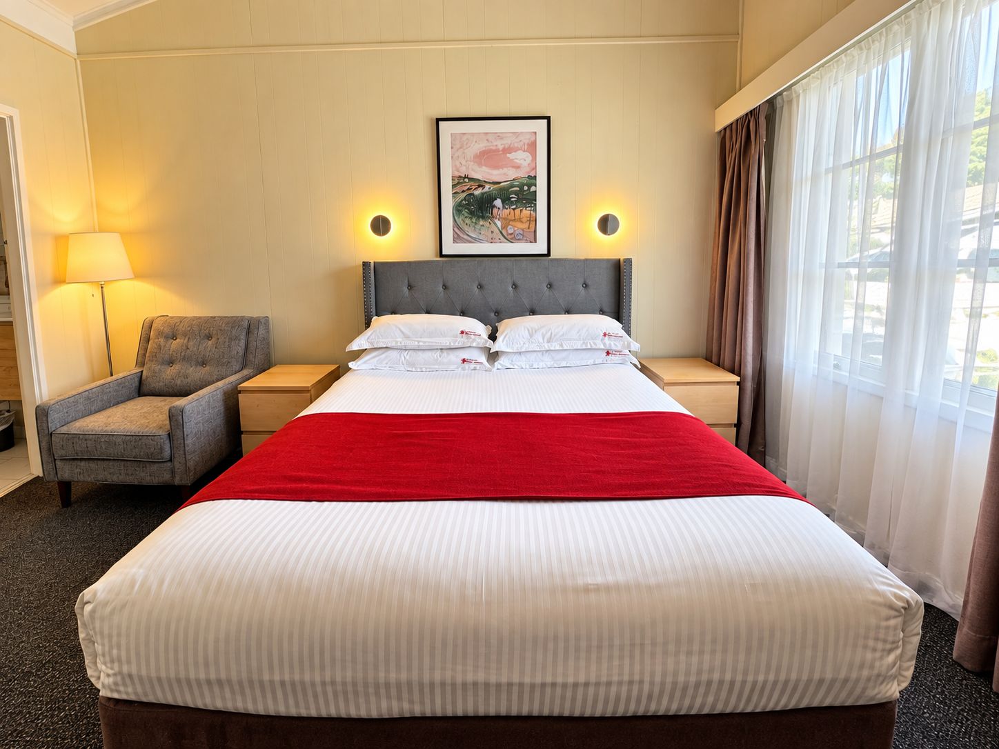 A hotel room with a large bed, two bedside tables, a chair, a framed picture on the wall, and a window with curtains.