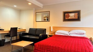 Ein Hotelzimmer mit Bett, Schreibtisch, Stuhl, Nachttisch, Spiegel und einem gerahmten Bild an der Wand.