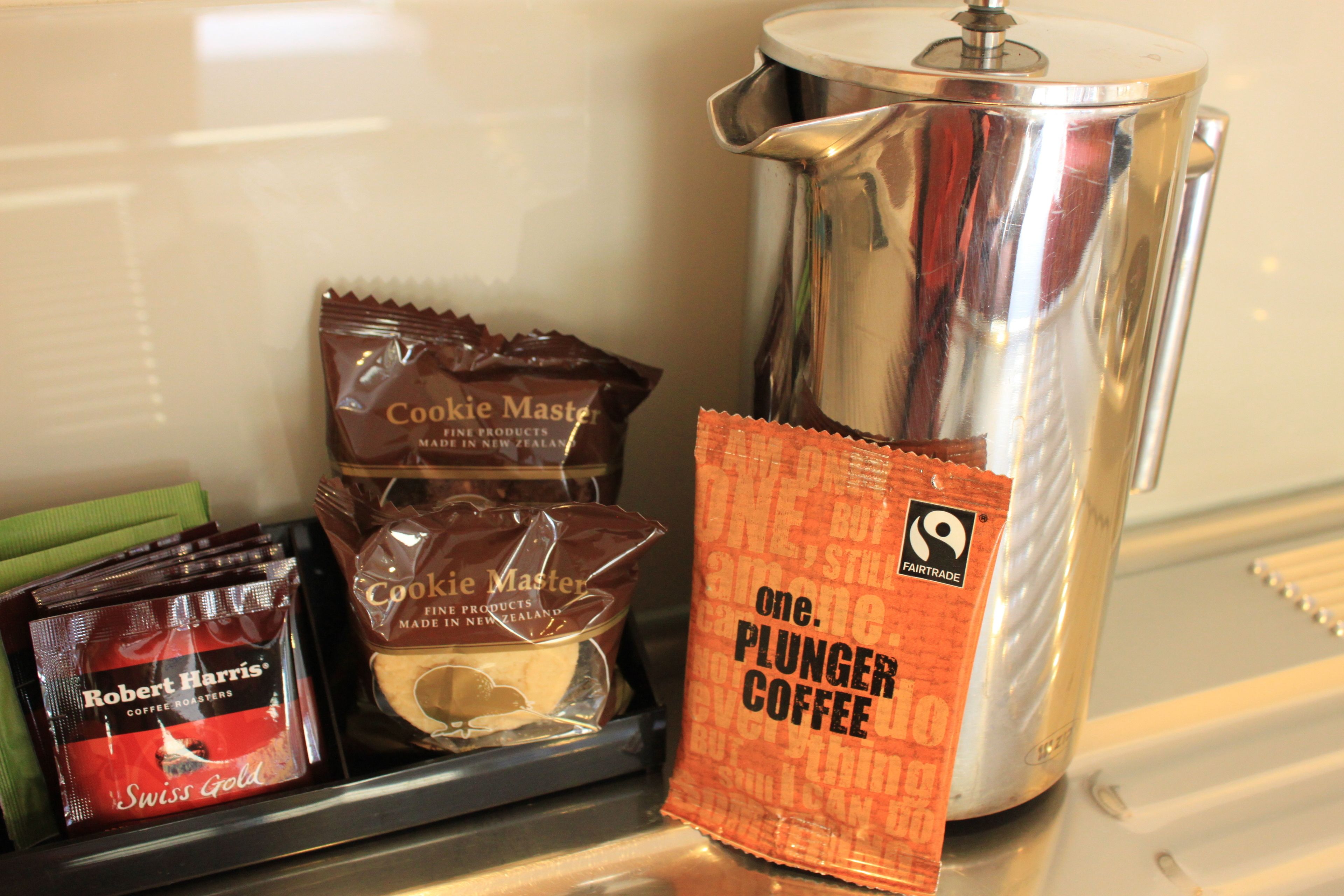 A coffee maker, a packet of Coffee Master, a packet of Robert Harris Swiss Gold, and a packet of Plunger Coffee on a counter.