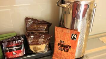 A coffee maker, a packet of Coffee Master, a packet of Robert Harris Swiss Gold, and a packet of Plunger Coffee on a counter.