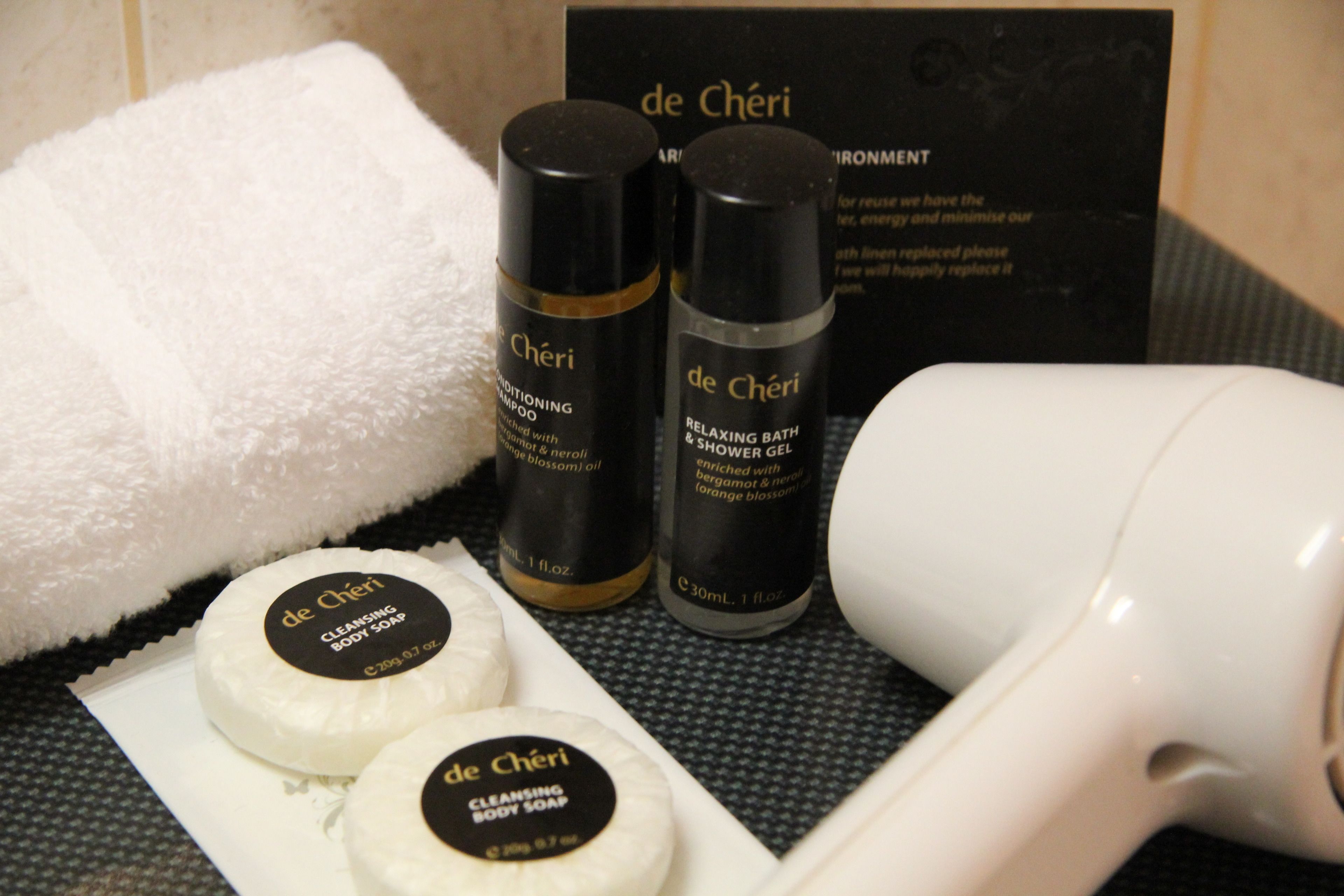 A set of toiletries including body soap, shampoo, and a relaxing bath gel, along with a white towel and a hairdryer.