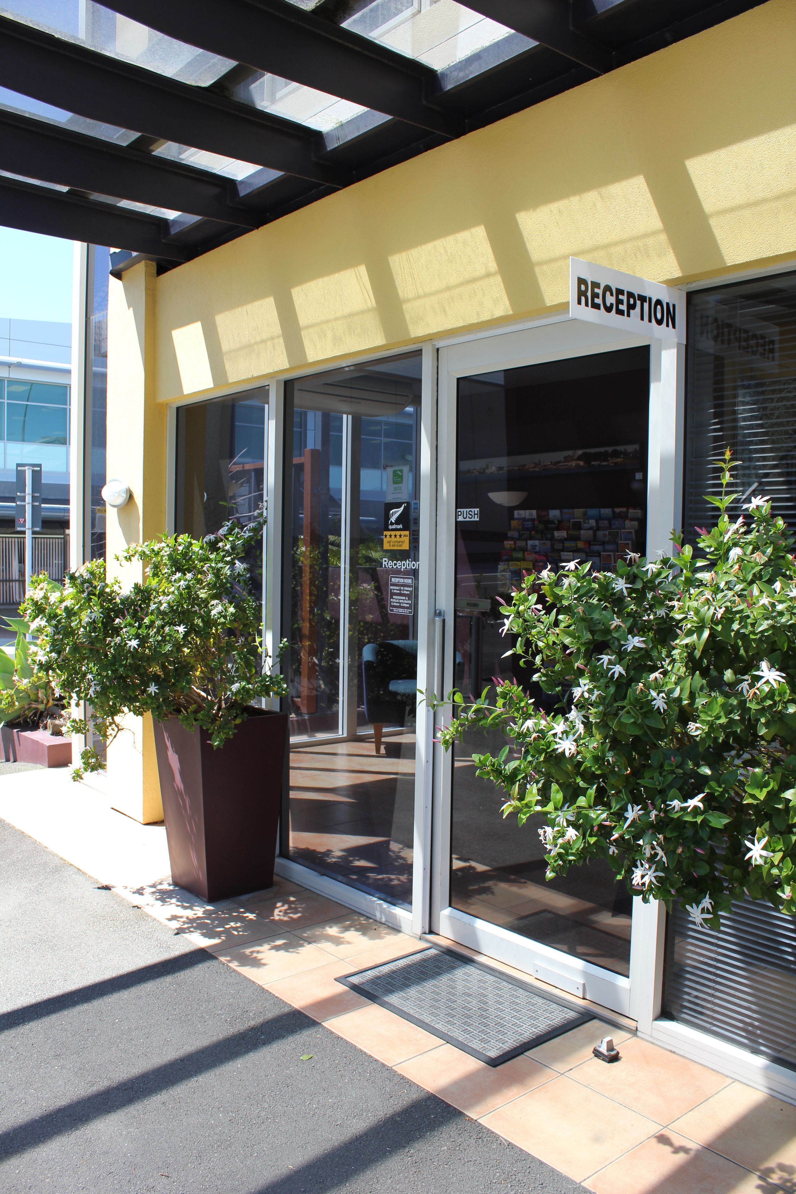 Un espace d’accueil doté d’une porte en verre, d’une enseigne au-dessus et de deux plantes en pot à l’extérieur.