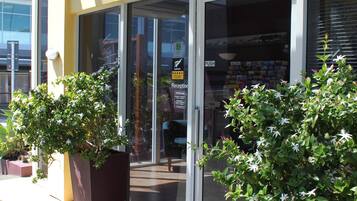 Un espace d’accueil doté d’une porte en verre, d’une enseigne au-dessus et de deux plantes en pot à l’extérieur.