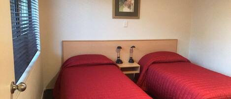 A room with two single beds, each with red bedding, a wooden headboard, and a small bedside table with two black lamps.