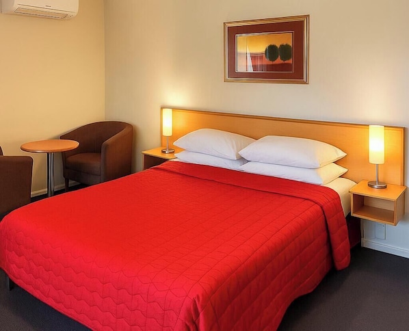 A hotel room with a large bed, two bedside lamps, a chair, and a framed picture on the wall. - Harbour City Motor Inn (Tauranga)