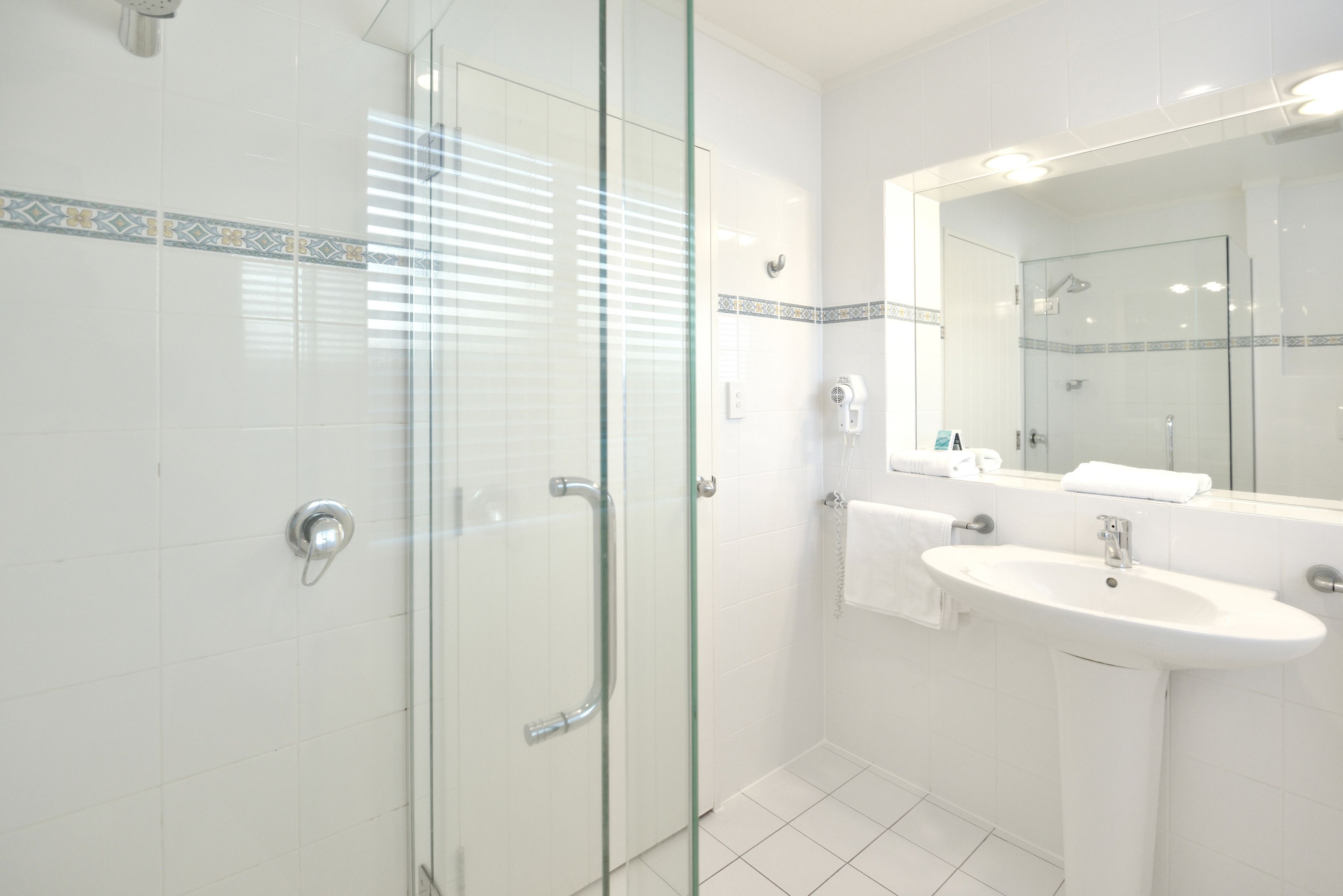 A modern bathroom with a glass shower enclosure, a sink with a mirror, and a tiled floor.