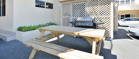 A wooden picnic table with benches, a barbecue grill, and a lattice fence in a residential area.