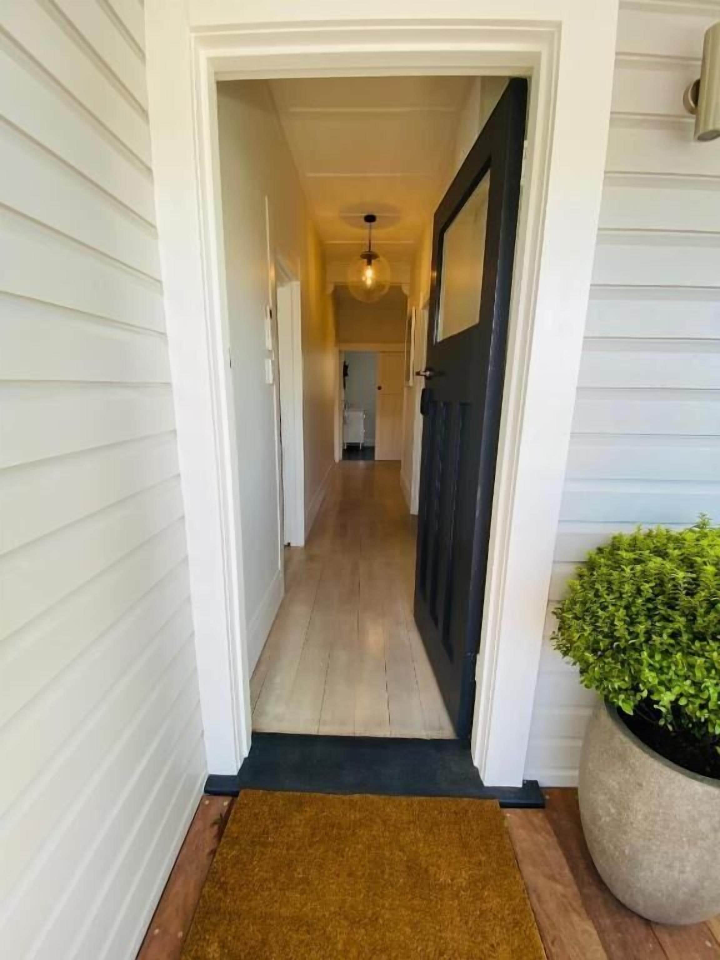 A hallway with white siding, a dark door, and a potted plant.