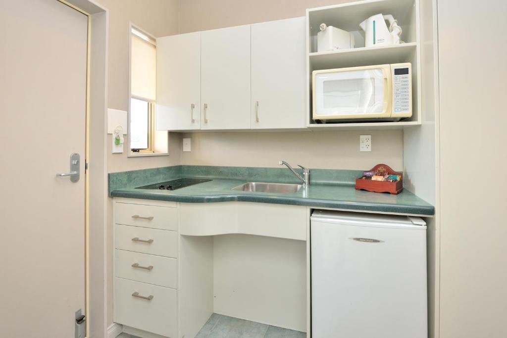 Una cocina compacta con armarios blancos, un microondas integrado y un refrigerador pequeño.