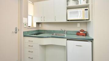 Una cocina compacta con armarios blancos, un microondas integrado y un refrigerador pequeño.