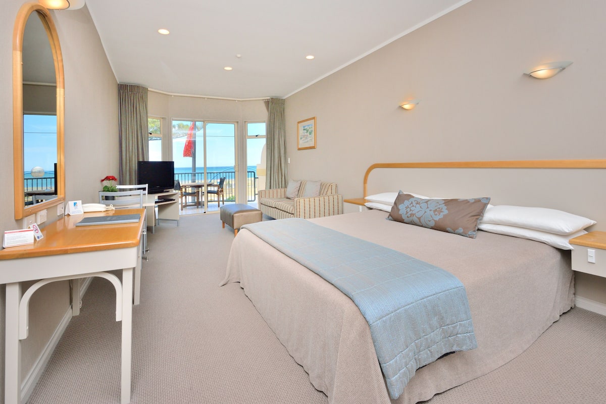 Habitación de hotel con una cama grande, un escritorio con computadora, televisión y un balcón con vista al mar.
