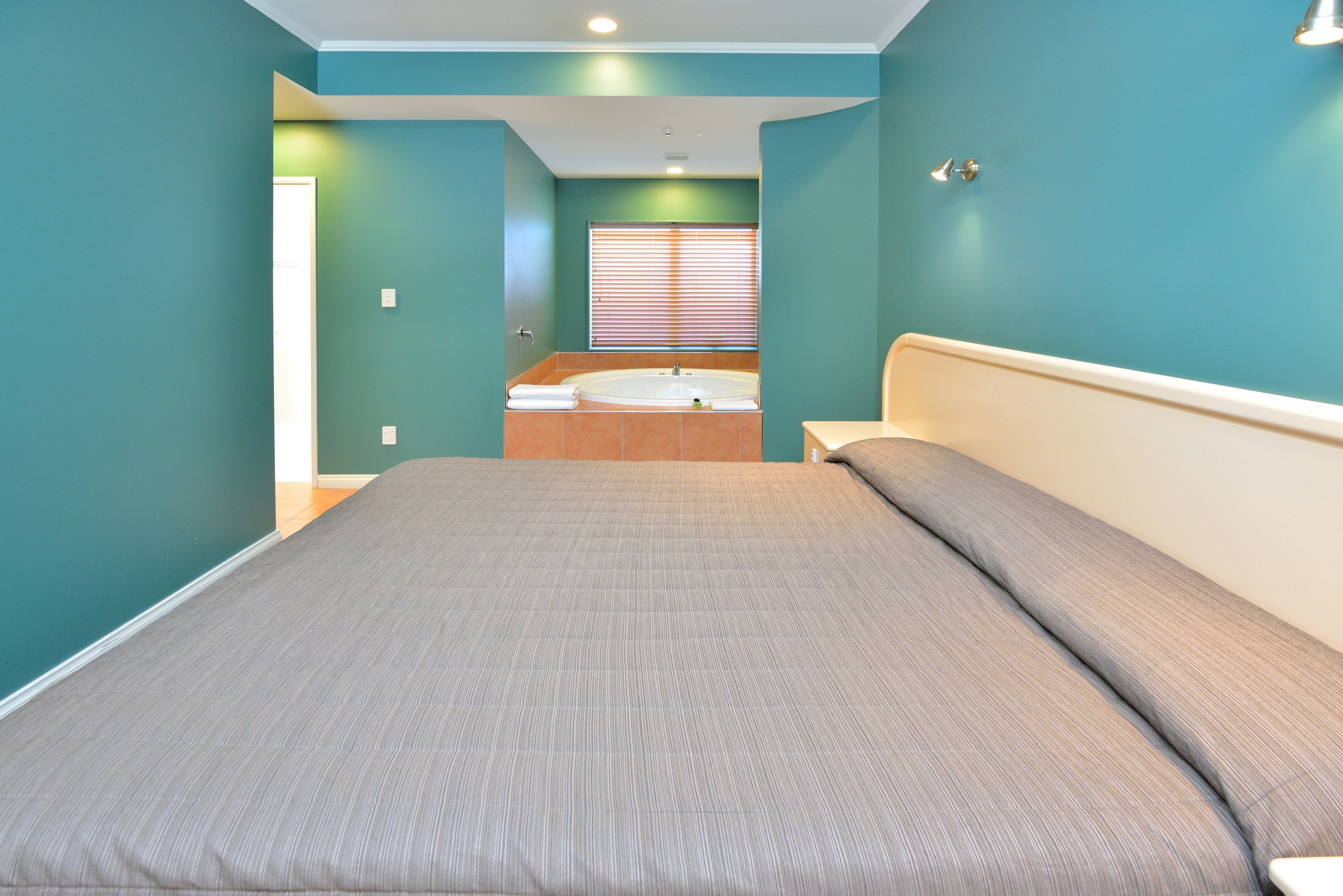 A bedroom with a large bed, a bathroom with a bathtub, and teal walls.