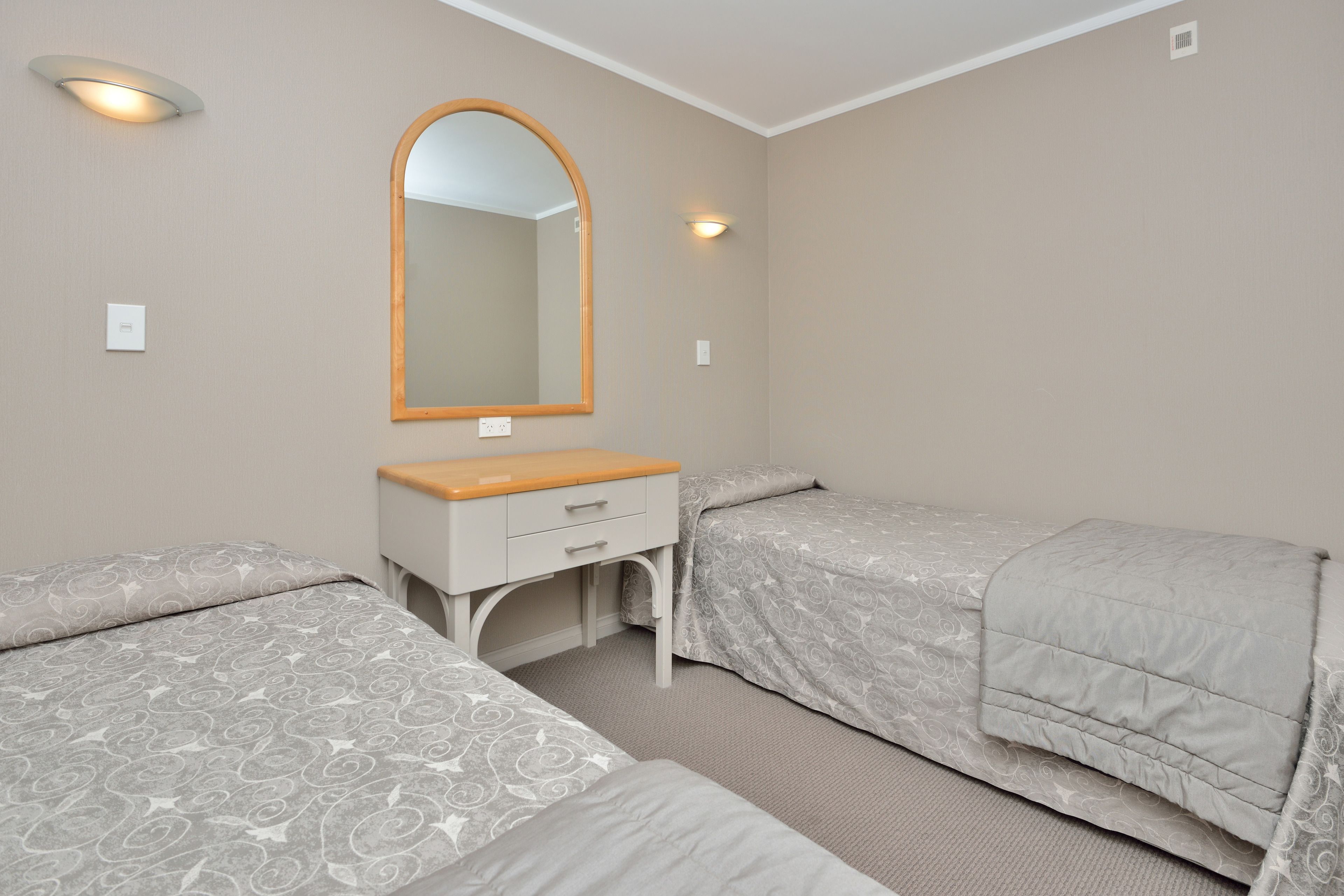 A bedroom with two single beds, a wooden dresser, a large mirror, and a light fixture above the dresser.