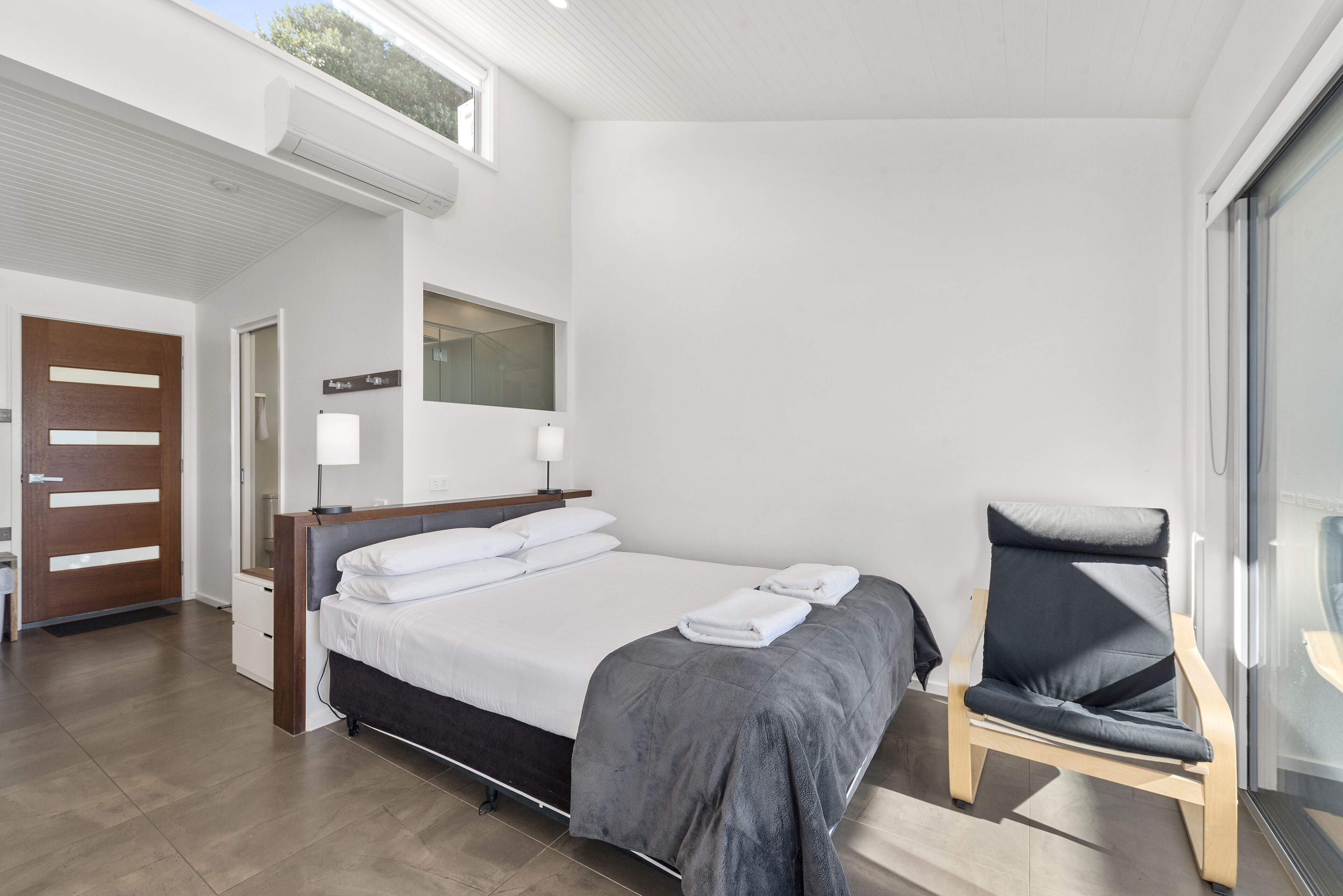 A modern hotel room with a large bed, a chair, and a large window.