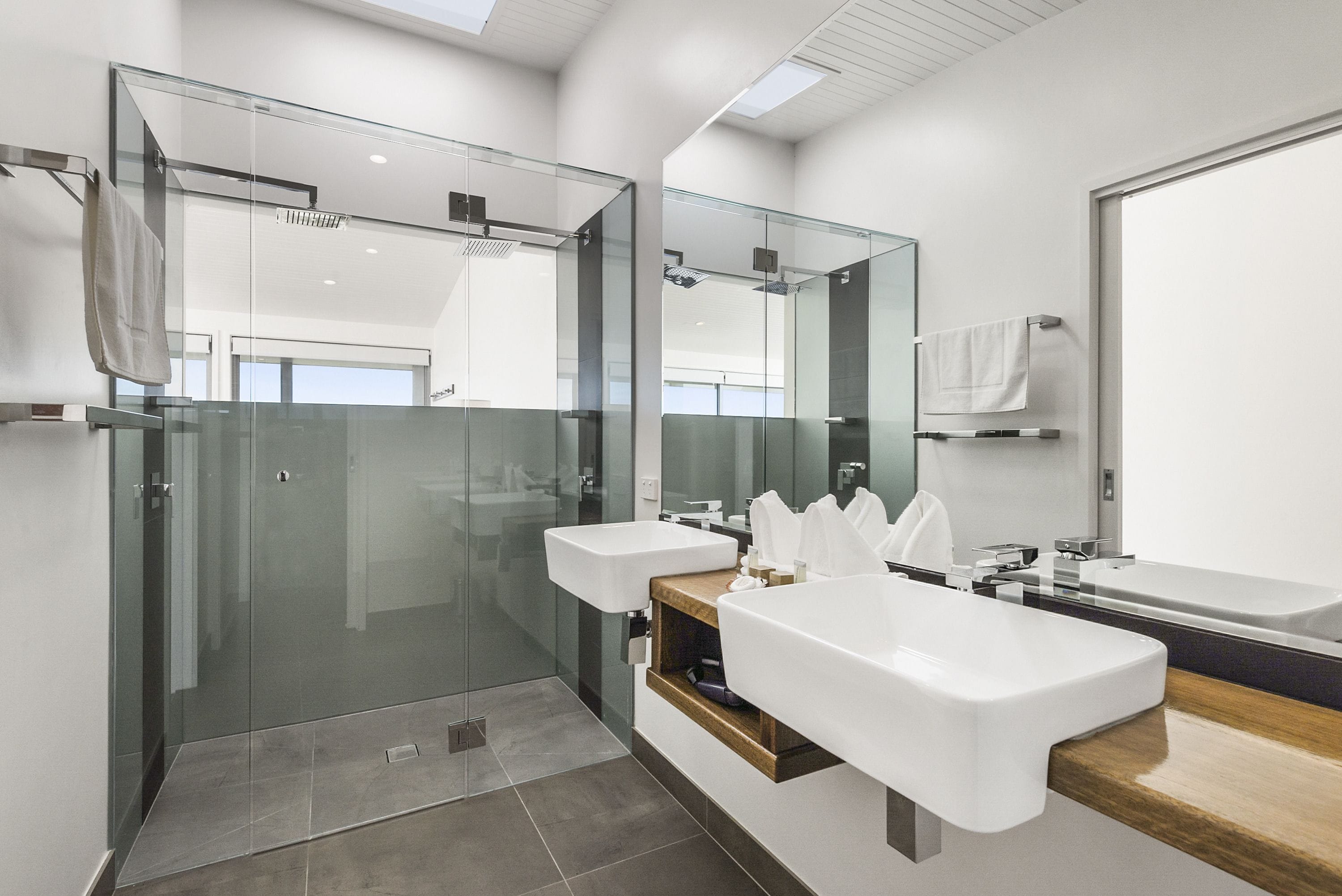 A modern bathroom with two sinks, a glass shower enclosure, and a large mirror.