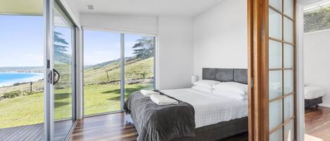 Una camera da letto con un letto grande, una porta scorrevole in vetro che dà su un balcone con vista sul mare e un pavimento in legno.