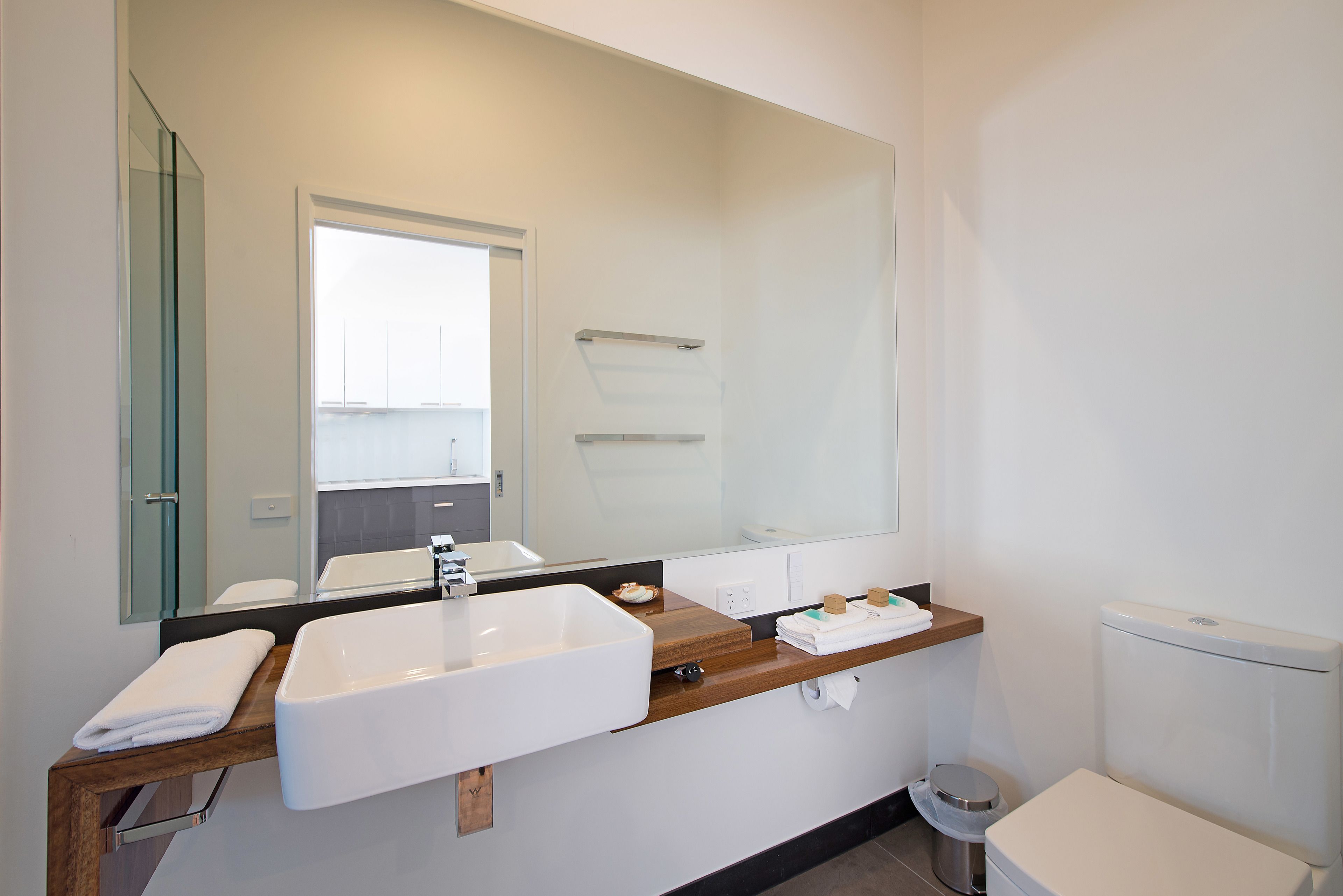 A modern bathroom with a large mirror, a white sink, a wooden countertop, and a toilet.