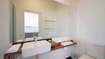 A modern bathroom with a large mirror, a white sink, a wooden countertop, and a toilet.