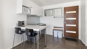A compact kitchen with a white countertop, stainless steel appliances, and a wooden door. - Seafarers Getaway (Apollo Bay)