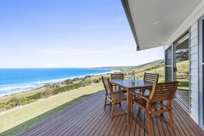A wooden deck with a table and chairs overlooking a coastal landscape. - Seafarers Getaway (Apollo Bay)