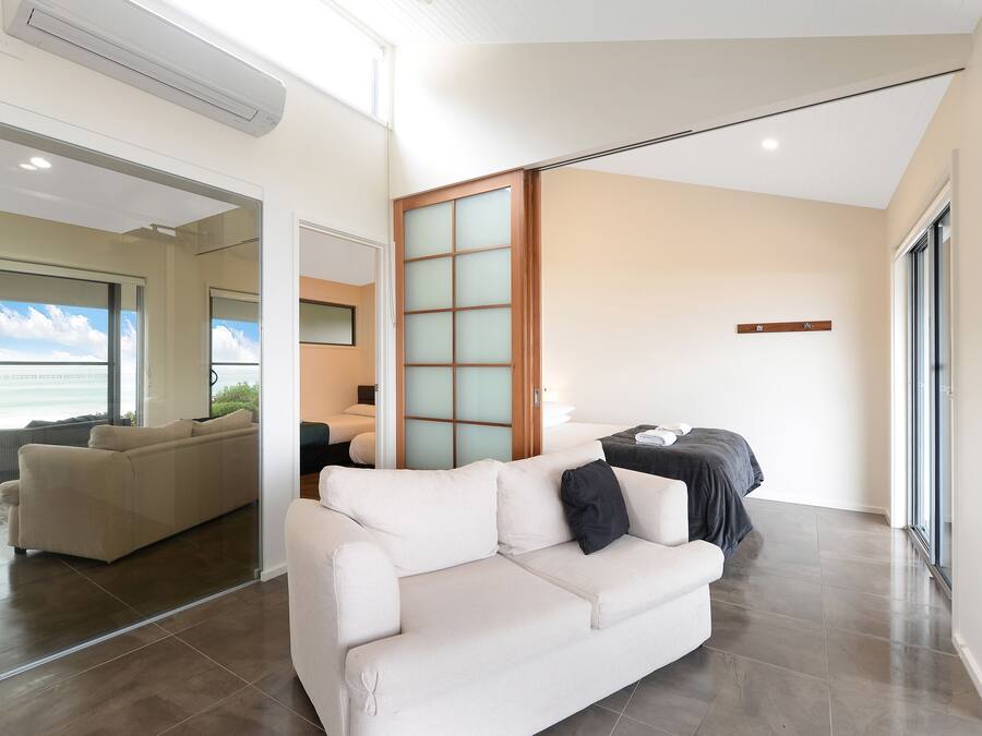Ein modernes Wohnzimmer mit Sofa, Bett und einer Glasschiebetür, die auf einen Balkon führt.