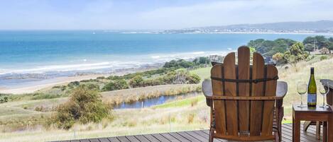 A wooden deck with a wooden chair facing a coastal view.