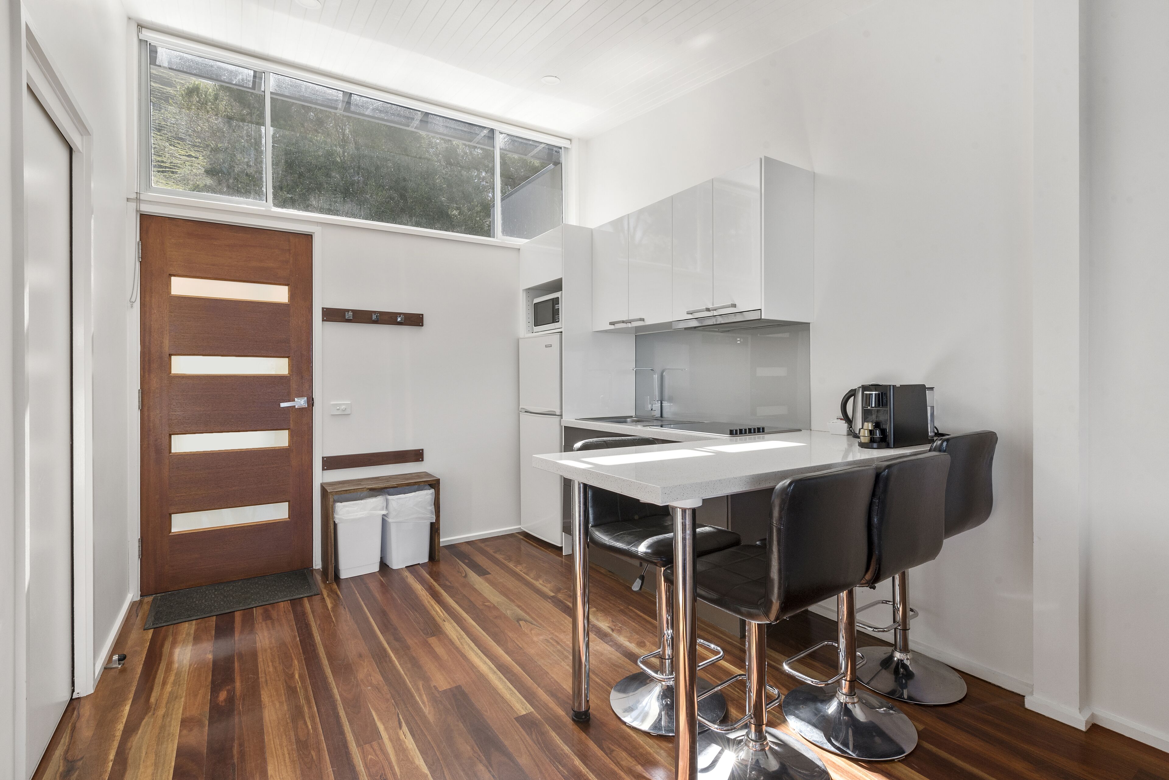 A modern kitchen with a wooden door, white cabinets, a stainless steel bar stool, and a small countertop.