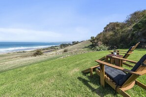 A grassy area with a wooden chair and table, overlooking a beach and ocean.