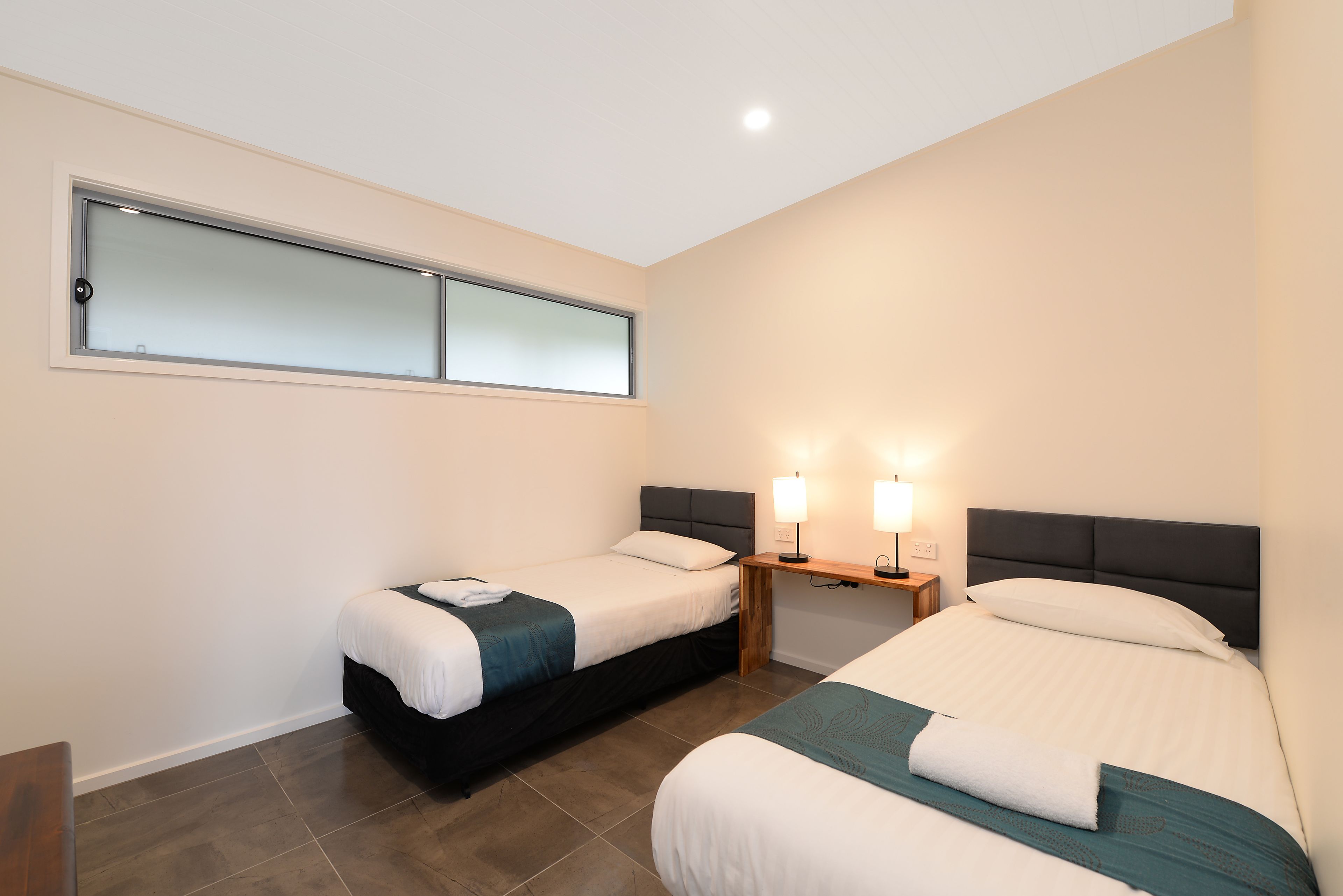 Een hotelkamer met twee bedden, een klein tafeltje met lampen en een raam met gezandstraald glas.