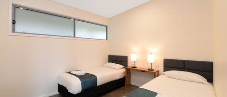 A hotel room with two beds, a small table with lamps, and a window with frosted glass.