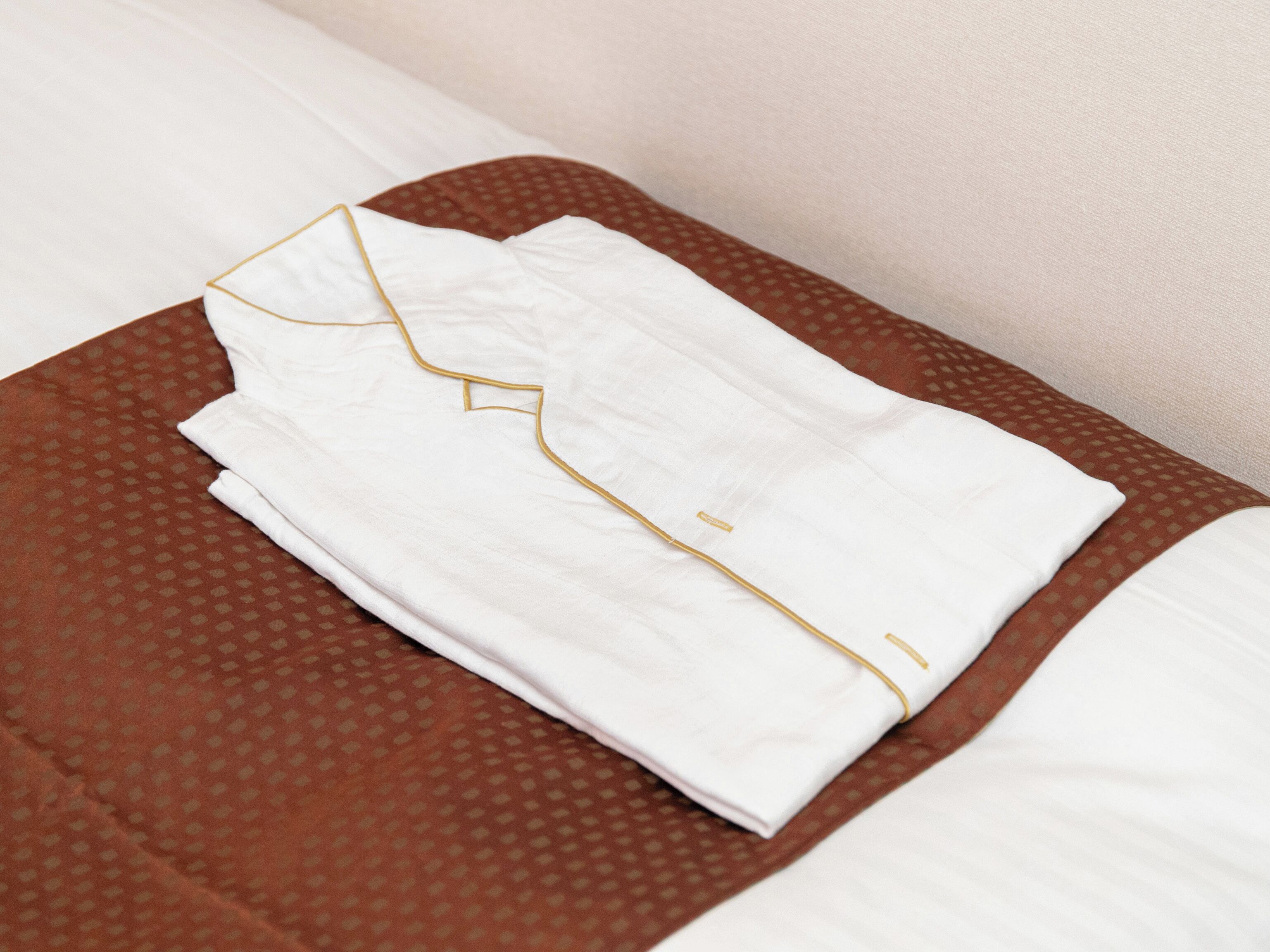Una camisa blanca bien doblada con detalles dorados sobre una colcha marrón estampada.