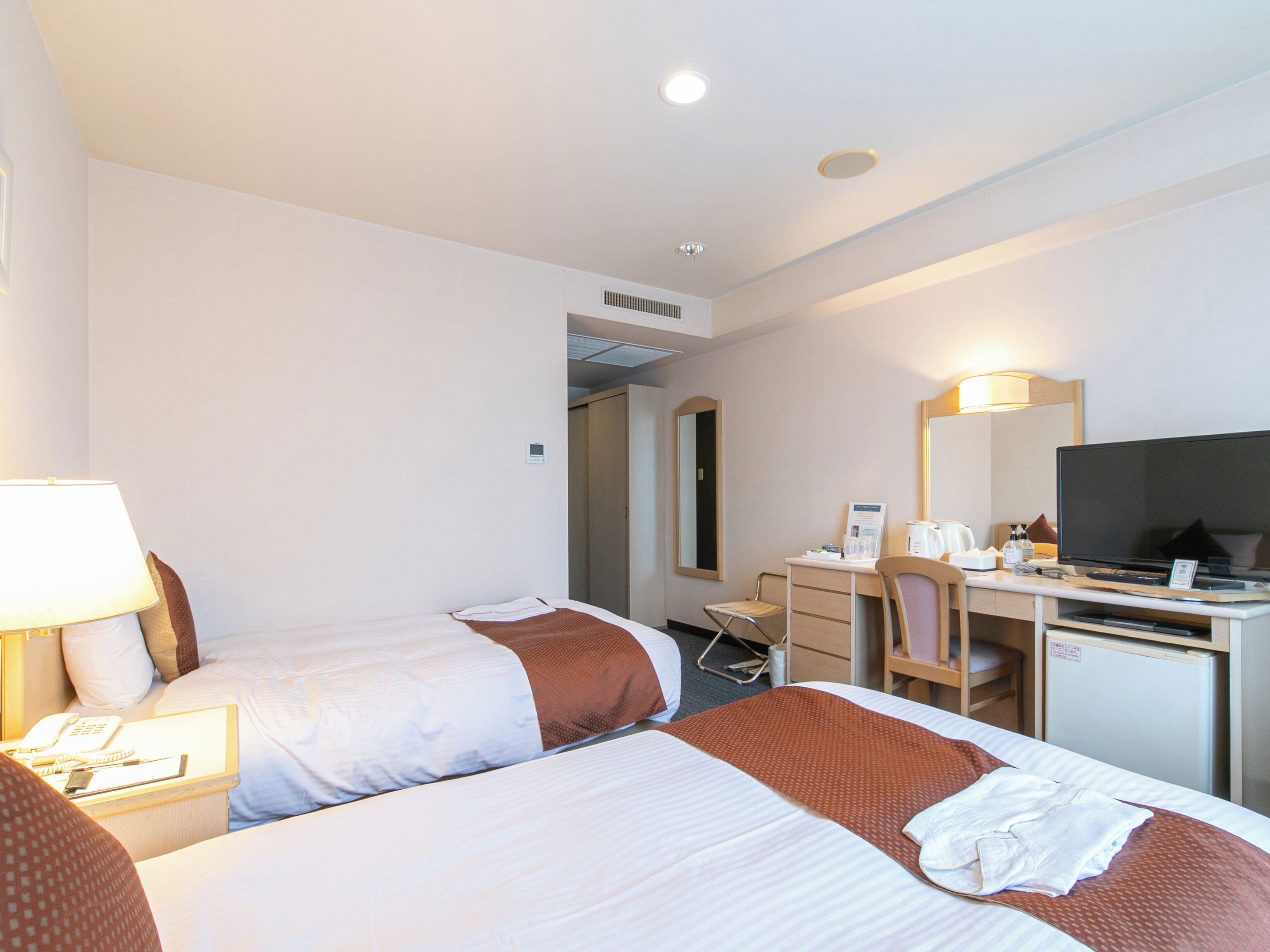 A hotel room with two beds, a desk, a chair, a television, and a mirror.