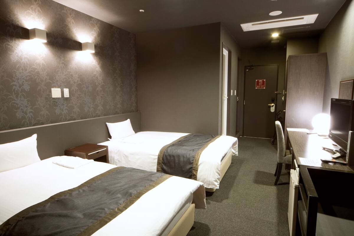 Een hotelkamer met twee bedden, een bureau, een stoel en een televisie.