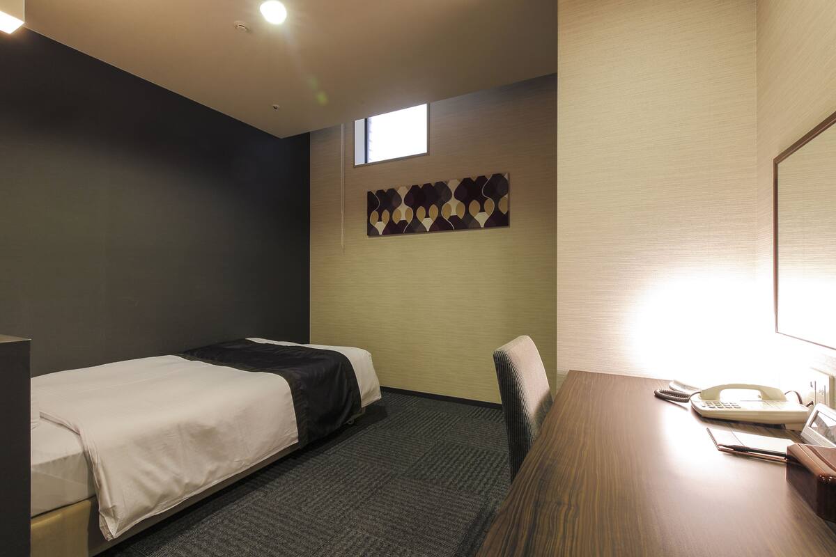 Een hotelkamer met twee bedden, een bureau met telefoon en een klein raam.