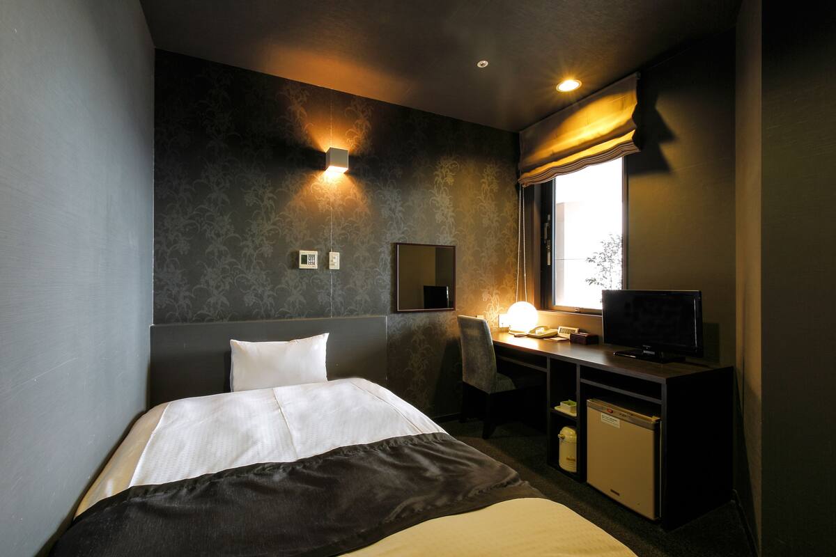 Een hotelkamer met een bed, bureau, stoel, televisie en een raam met gordijnen.