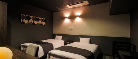 Ein Hotelzimmer mit zwei Betten, einem Schreibtisch, einer Lampe und einem an der Wand hängenden Kunstwerk.