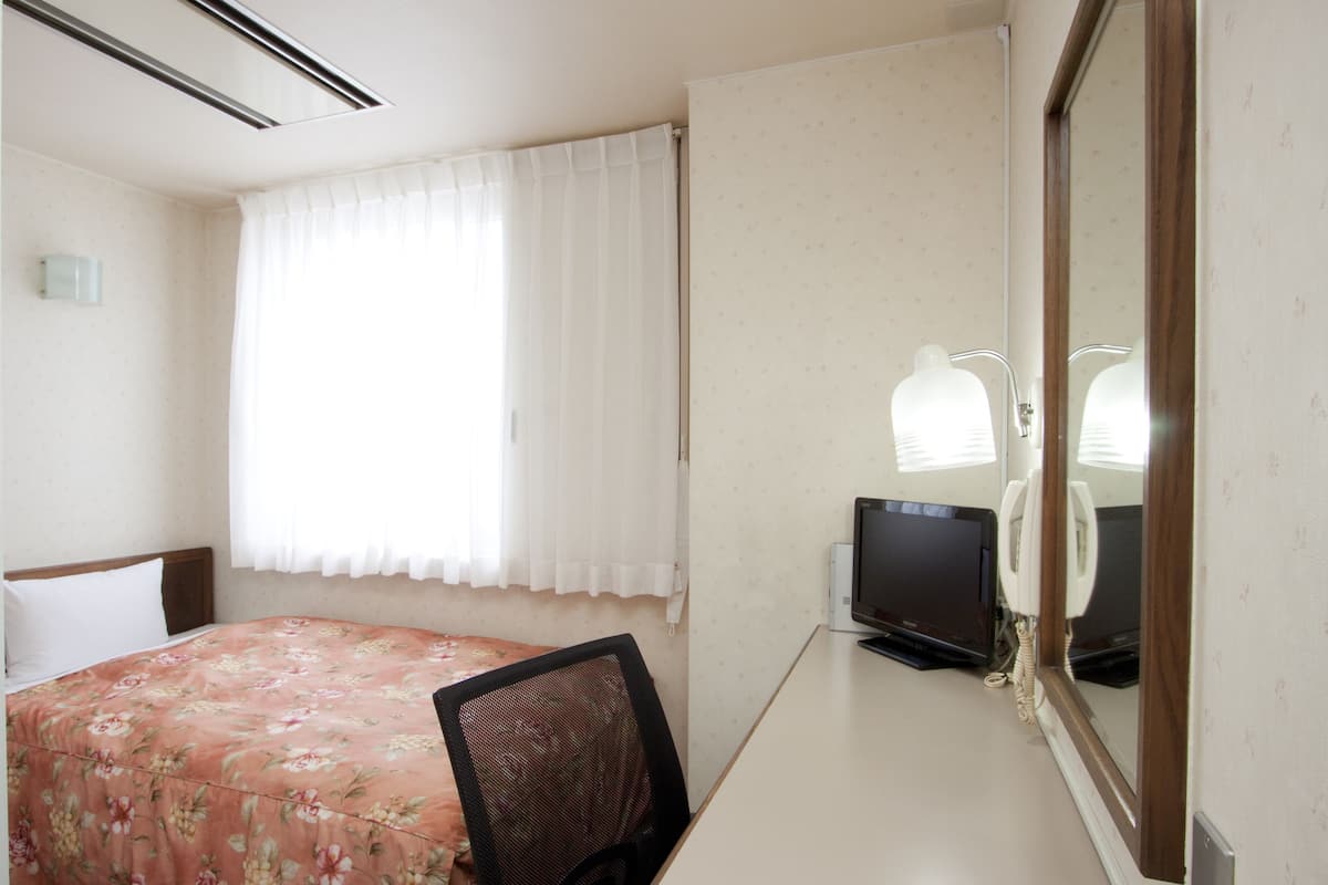 Ein Hotelzimmer mit einem Bett, einem Schreibtisch mit Computer und Telefon, einem Stuhl und einem Fenster mit Vorhängen.