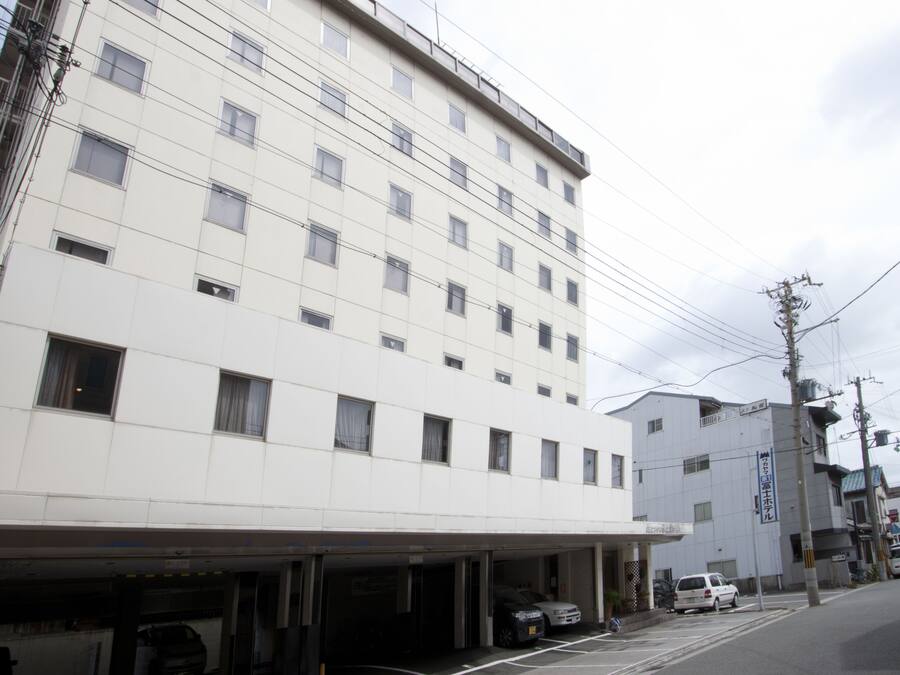 Um edifício de vários andares com fachada plana, diversas janelas e área de estacionamento na frente.