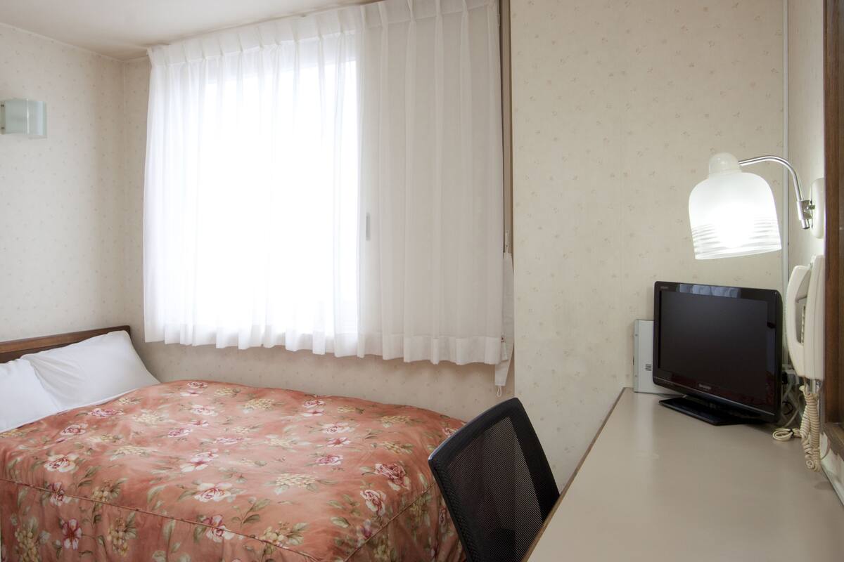 Ein Hotelzimmer mit einem Bett, einem Schreibtisch mit Computerbildschirm und einem Telefon.