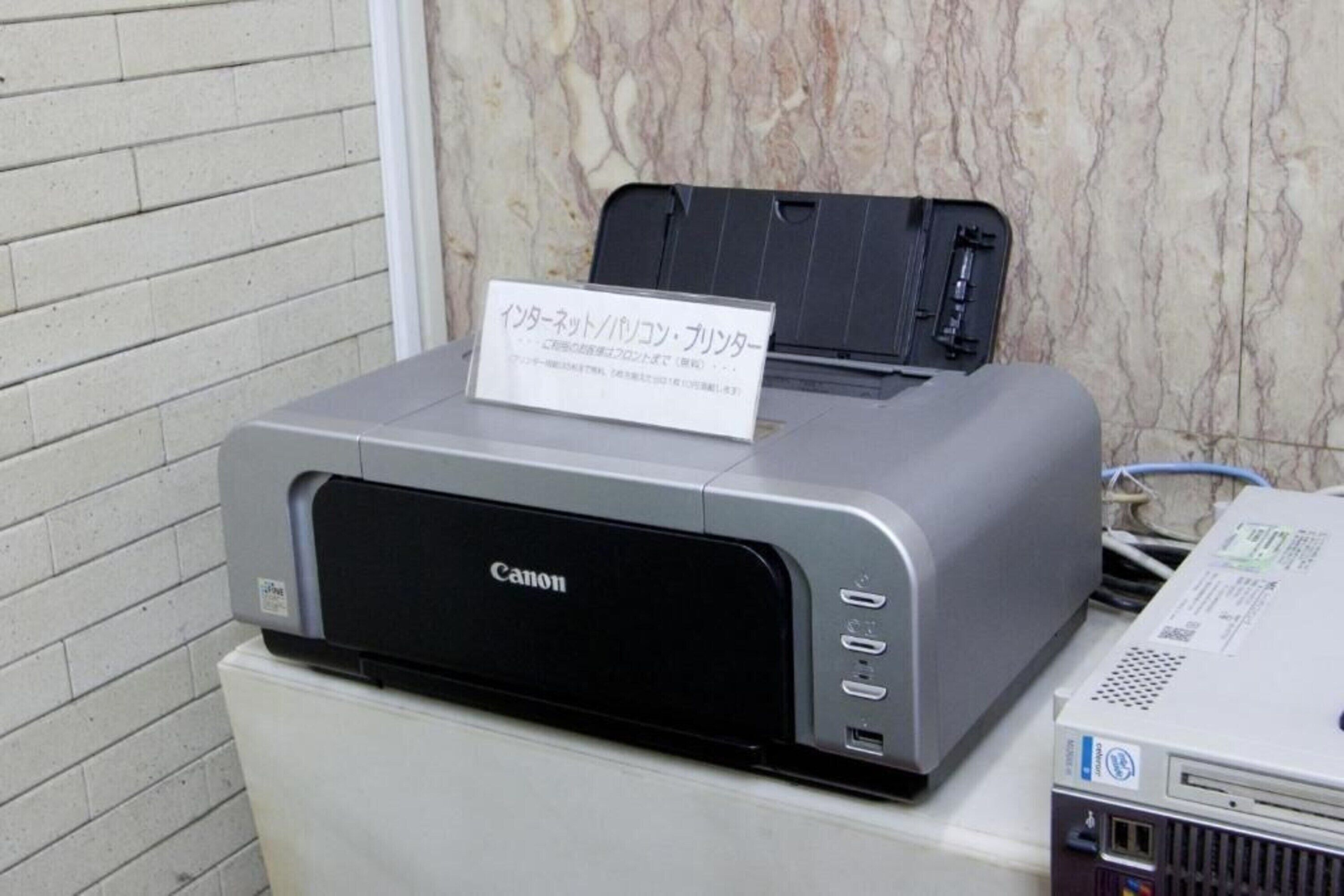 A Canon printer on a white pedestal with a sign in Japanese.