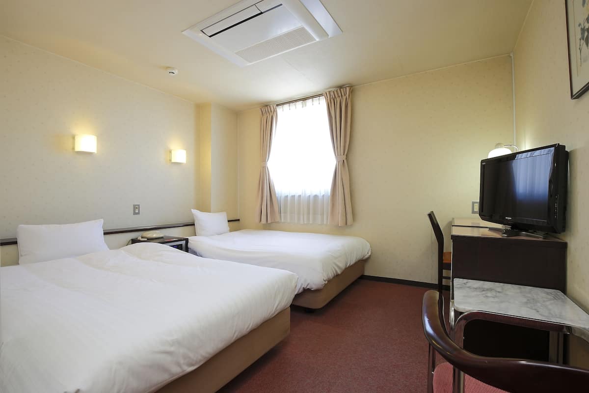 Een hotelkamer met twee bedden, een bureau met een televisie en een stoel.