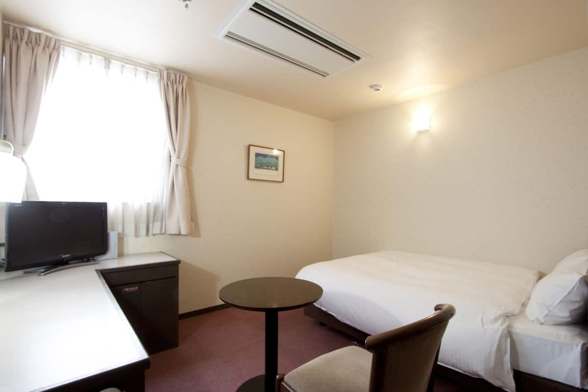 Een hotelkamer met een bed, een bureau met een televisie, een klein tafeltje en een stoel.