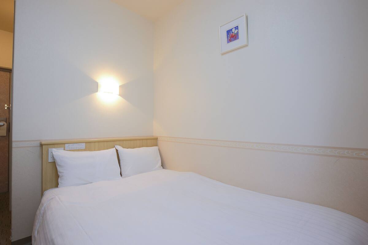 Een hotelkamer met een net opgemaakt bed, een wandlamp en een klein, ingelijst foto.