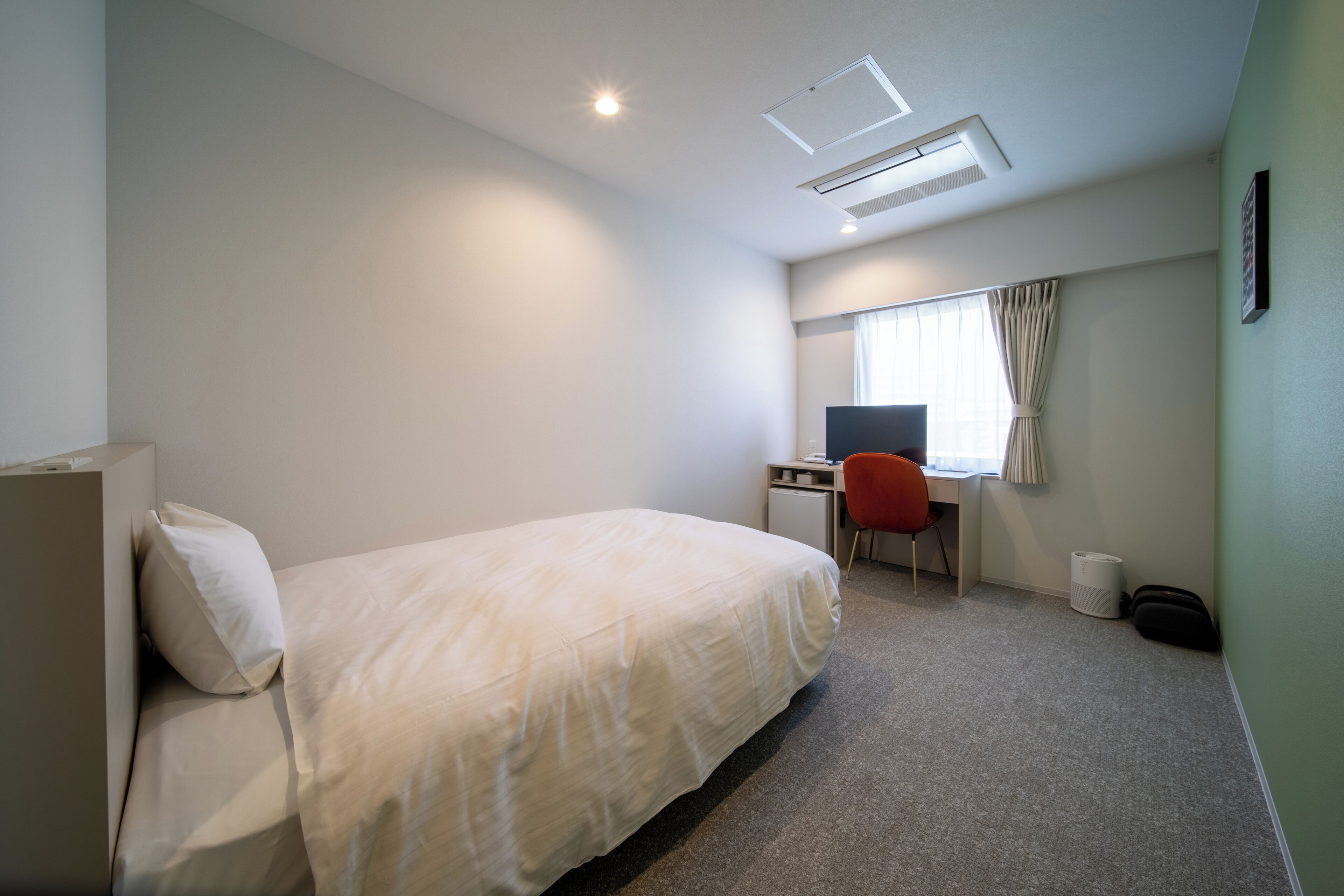 Habitación de hotel con cama, escritorio, silla, ventana con cortinas e iluminación en el techo.
