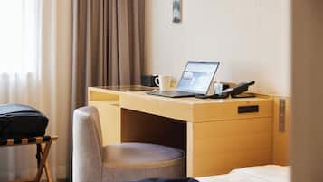 A hotel room with a wooden desk, a laptop, a telephone, and a cup.