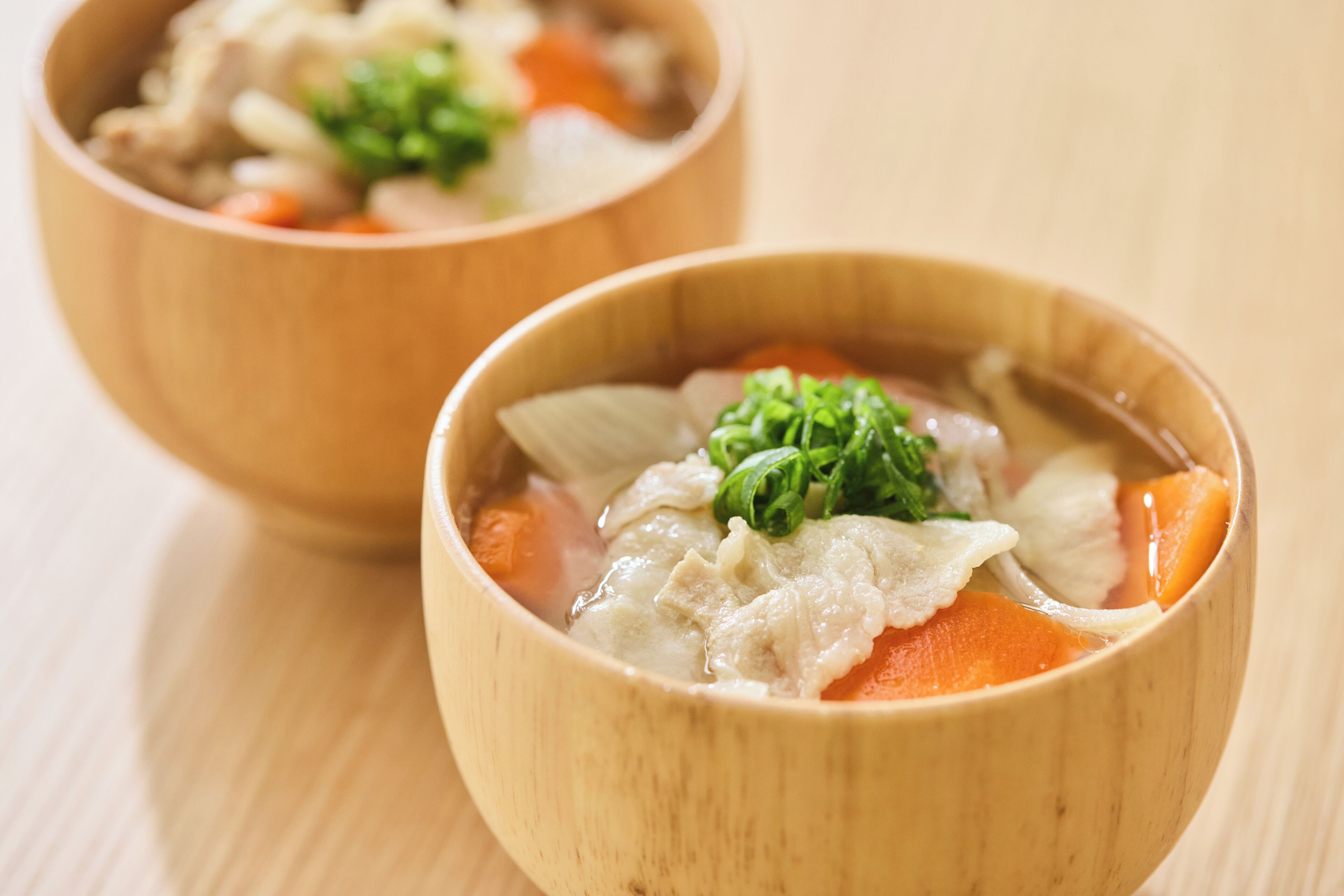 Dos tazones de madera con sopa de verduras y una guarnición.