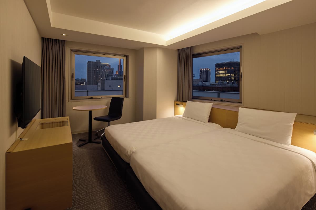 Hotelkamer met een groot bed, een bureau, een stoel, een televisie en twee ramen met uitzicht op de stad.
