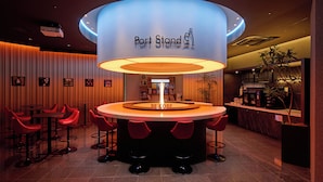 Un espace bar doté d’un comptoir circulaire, de tabourets de bar rouges et d’une enseigne indiquant « Port Stand ».