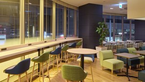 Un espace de détente intérieur moderne, doté de grandes fenêtres, d’un plancher en bois et d’un assortiment de fauteuils rembourrés aux couleurs vertes et bleues.