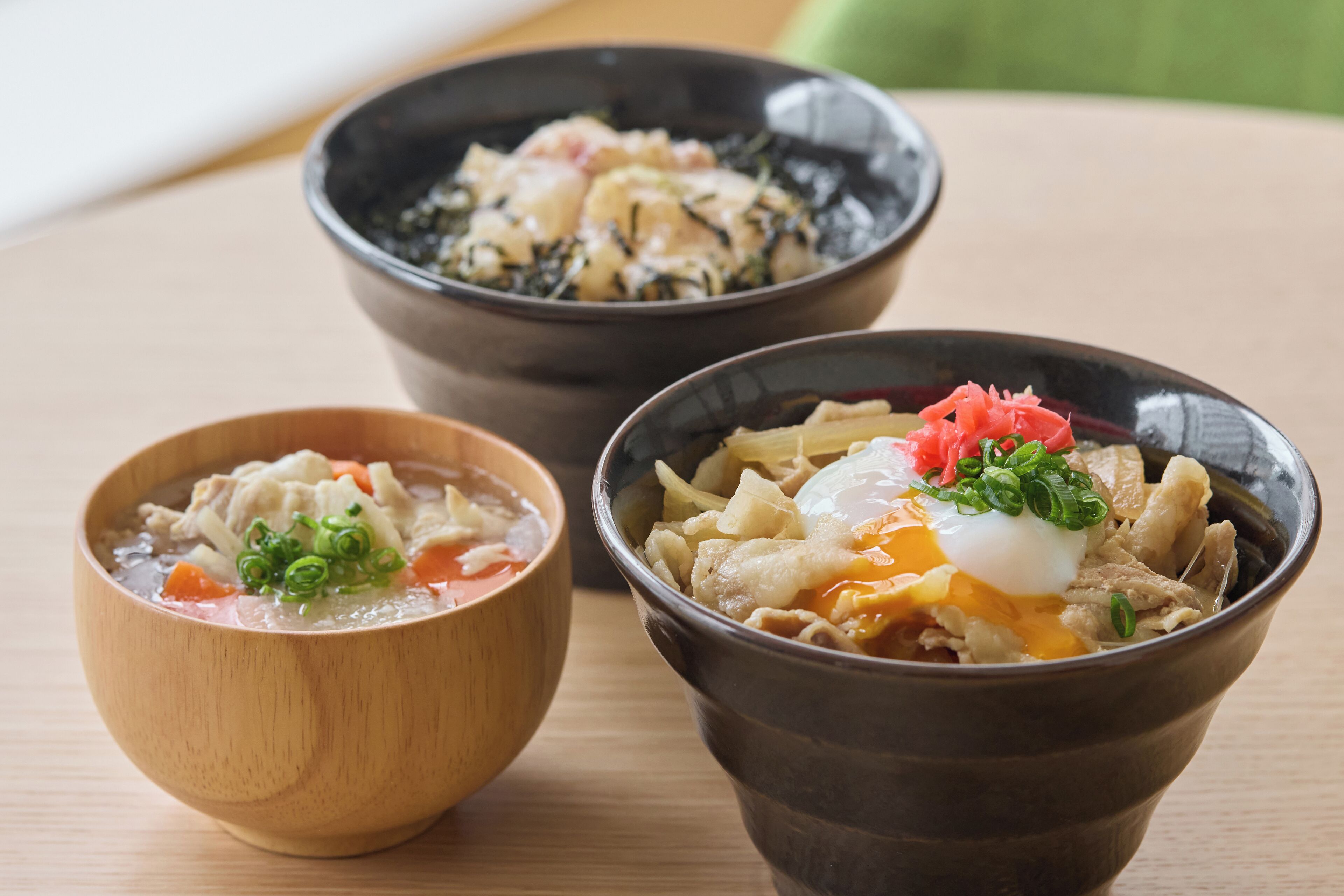Three bowls of soup with different toppings on a wooden table.